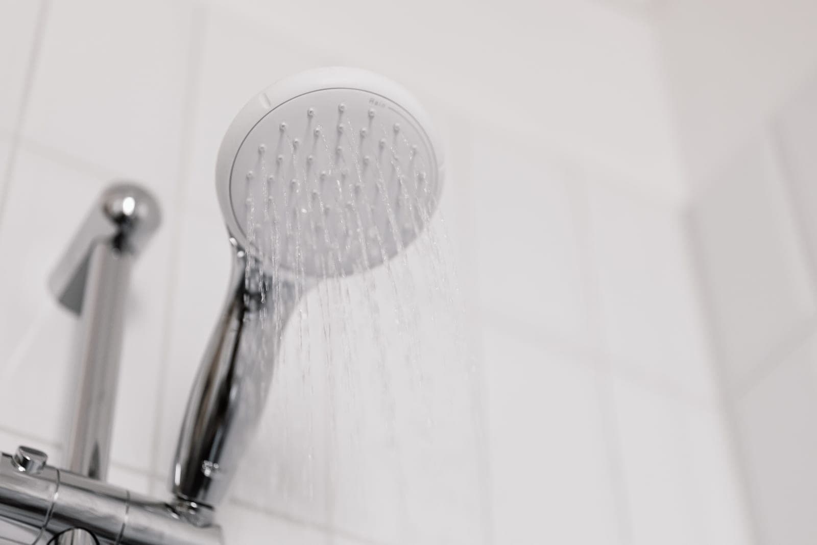 A chrome shower head spraying water in a tiled shower